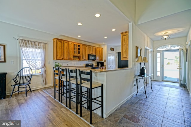 kitchen with glass insert cabinets, recessed lighting, a kitchen breakfast bar, brown cabinetry, and black appliances