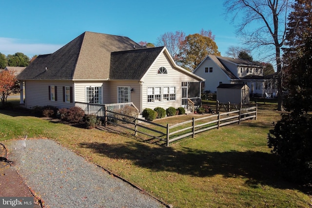 view of front facade with a shingled roof, a sunroom, a front yard, and fence