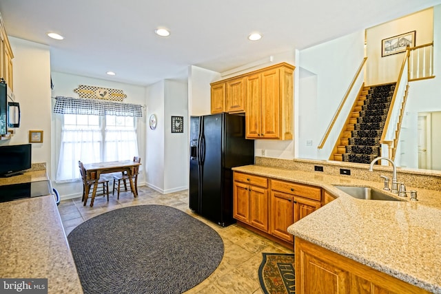 kitchen with recessed lighting, black fridge, light stone countertops, and a sink