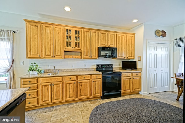 kitchen featuring black appliances, a sink, recessed lighting, glass insert cabinets, and light stone countertops