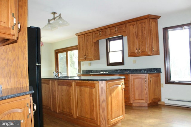 kitchen featuring black refrigerator, sink, dark stone counters, light hardwood / wood-style floors, and baseboard heating