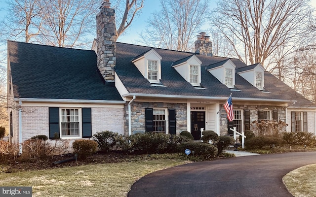 cape cod house featuring stone siding, a chimney, and roof with shingles