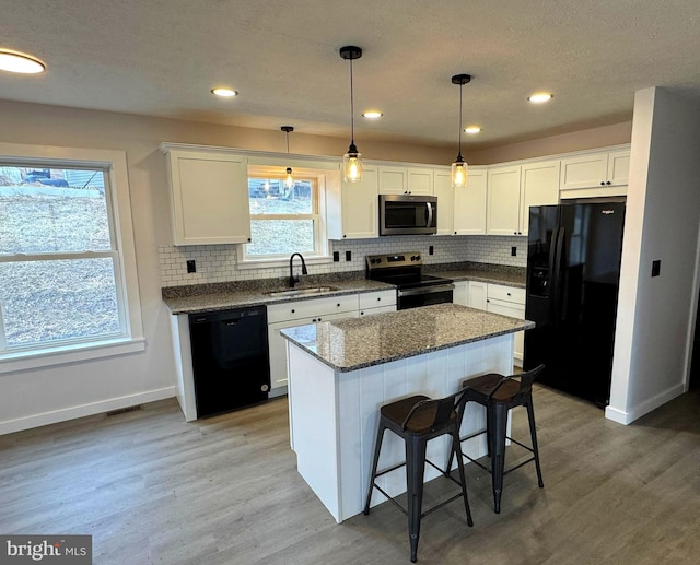 kitchen with sink, a center island, black appliances, white cabinets, and hanging light fixtures