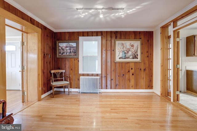 living area with light hardwood / wood-style flooring, crown molding, radiator, and wooden walls