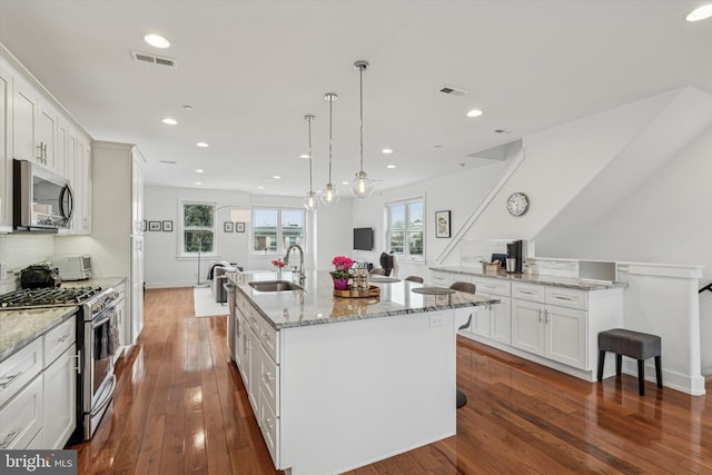 kitchen with stainless steel appliances, an island with sink, a sink, and visible vents