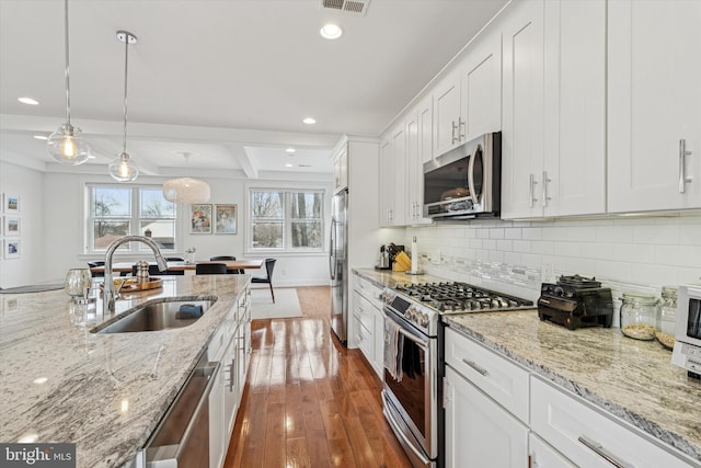 kitchen with tasteful backsplash, wood finished floors, stainless steel appliances, white cabinetry, and a sink