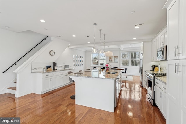 kitchen featuring light wood finished floors, visible vents, appliances with stainless steel finishes, a sink, and an island with sink