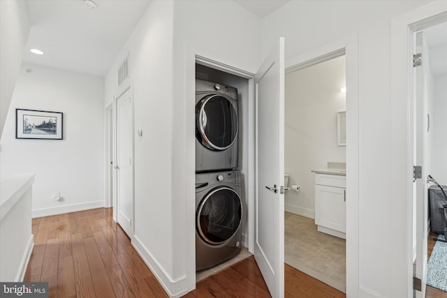 laundry room featuring light wood finished floors, visible vents, stacked washing maching and dryer, laundry area, and baseboards