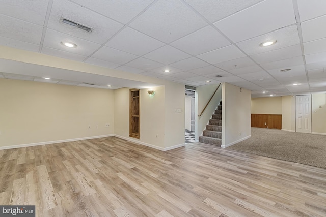 finished basement with light wood-style flooring, baseboards, visible vents, and stairway