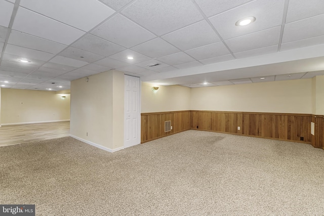 finished basement featuring visible vents, baseboards, a paneled ceiling, wainscoting, and light colored carpet