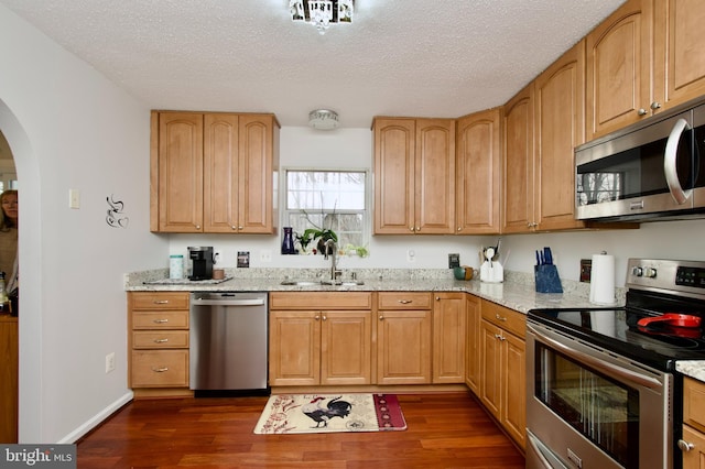 kitchen featuring stainless steel appliances, light stone counters, a textured ceiling, sink, and dark hardwood / wood-style floors