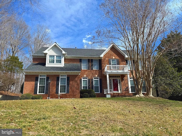 view of front facade with brick siding, a balcony, a front lawn, and roof with shingles