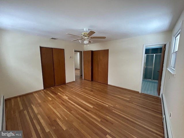 unfurnished bedroom with multiple closets, wood-type flooring, ceiling fan, and baseboard heating