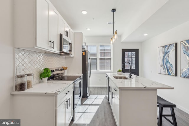 kitchen featuring stainless steel appliances, decorative backsplash, a sink, an island with sink, and light wood-type flooring