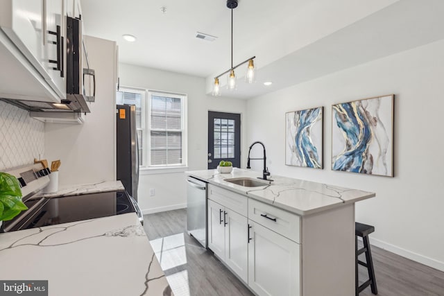 kitchen featuring visible vents, appliances with stainless steel finishes, white cabinetry, a sink, and an island with sink