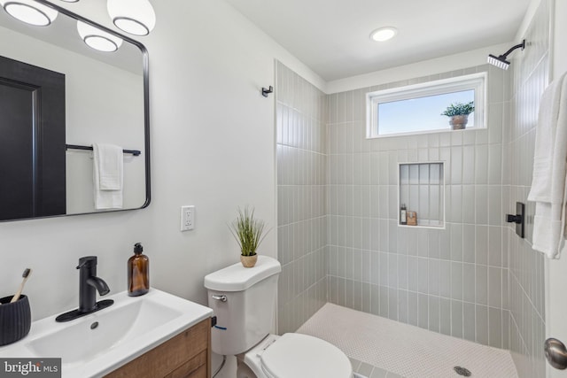 full bath featuring a tile shower, vanity, and toilet