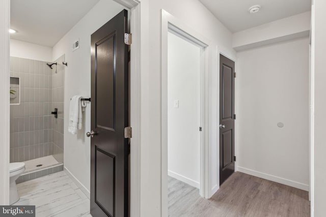 full bath with tiled shower, toilet, baseboards, and wood finished floors