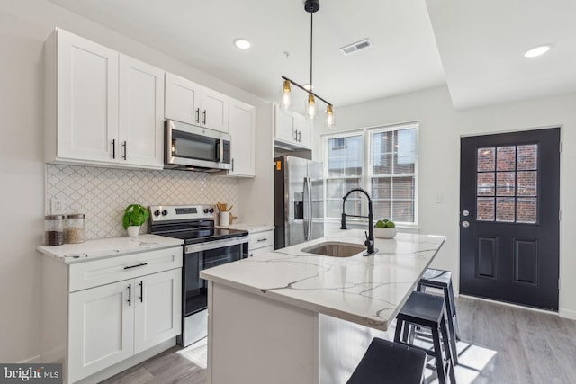 kitchen featuring light stone counters, stainless steel appliances, visible vents, light wood-style floors, and a sink