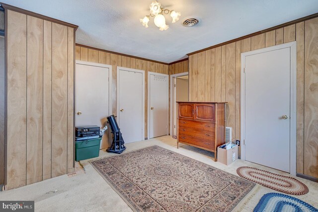 carpeted bedroom with crown molding, visible vents, and wood walls