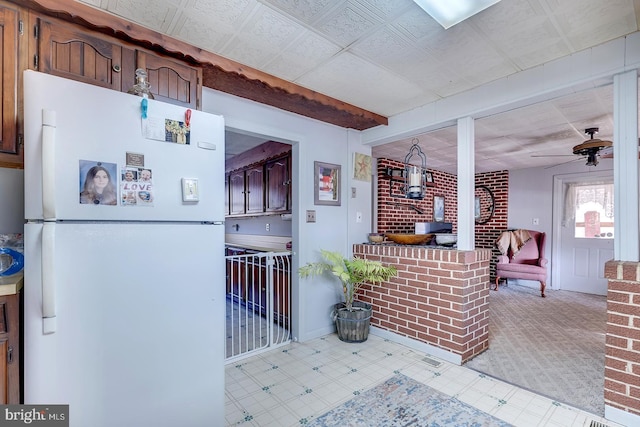 kitchen featuring tile patterned floors, brick wall, freestanding refrigerator, and ceiling fan