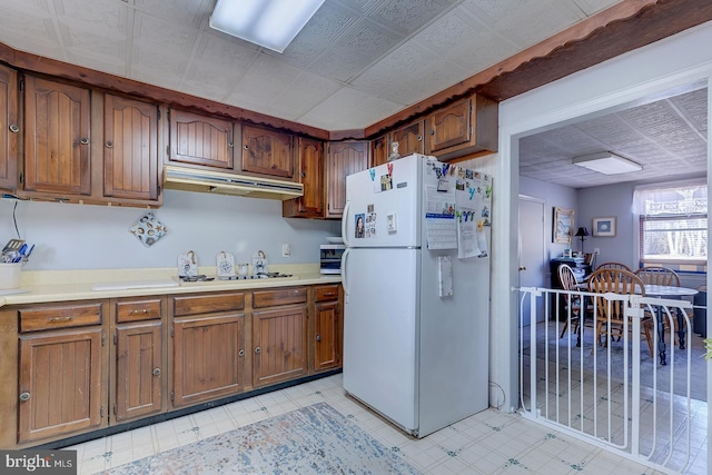 kitchen featuring under cabinet range hood, light floors, brown cabinetry, and freestanding refrigerator