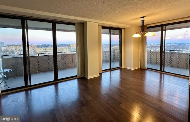 unfurnished room with a textured ceiling, a view of city, a notable chandelier, expansive windows, and dark wood finished floors