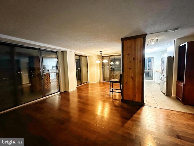 unfurnished room with a textured ceiling, light wood finished floors, rail lighting, and an inviting chandelier