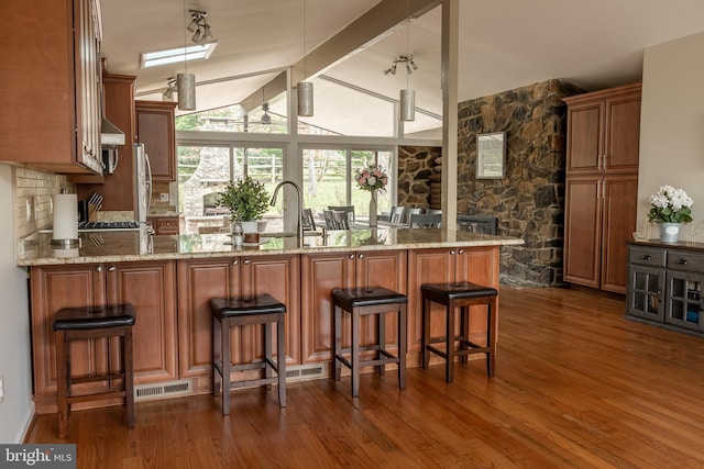 kitchen featuring light stone countertops, dark hardwood / wood-style floors, a kitchen bar, and kitchen peninsula