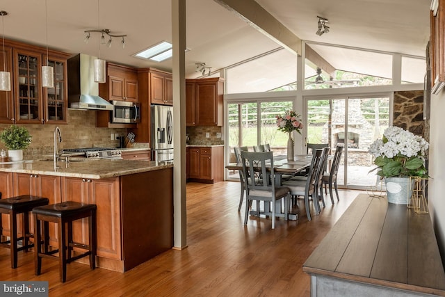 kitchen with dark wood-type flooring, sink, kitchen peninsula, stainless steel appliances, and wall chimney range hood