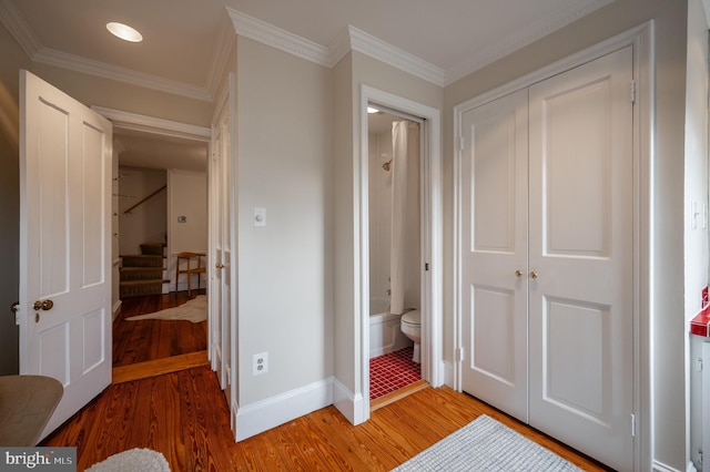 interior space with light wood-style floors, a closet, ensuite bath, ornamental molding, and baseboards