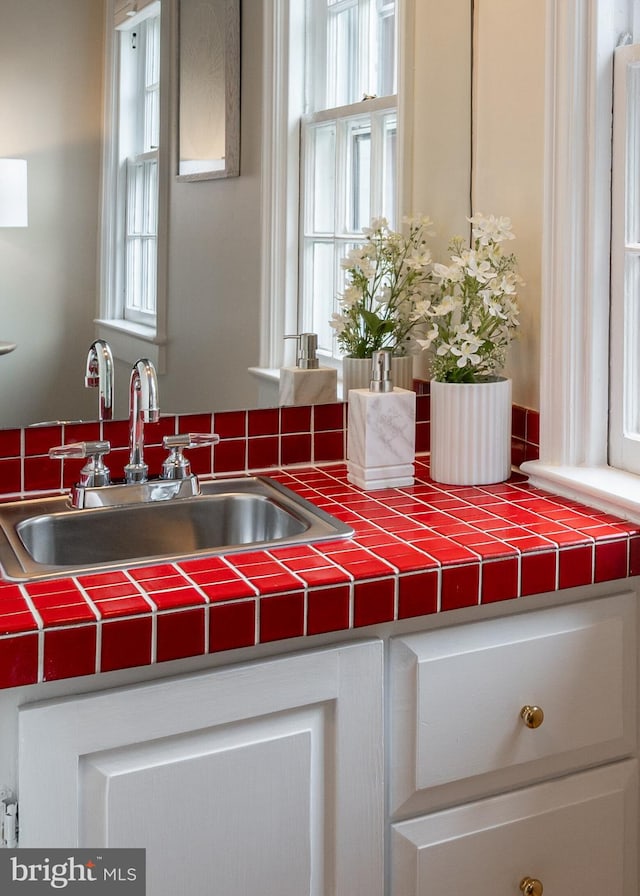 details featuring a sink, white cabinets, and tile countertops