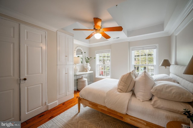 bedroom with visible vents, ceiling fan, light wood-type flooring, crown molding, and a tray ceiling