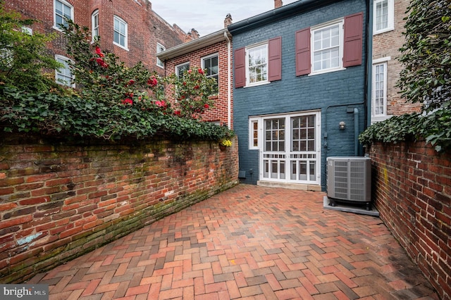 rear view of property with brick siding, cooling unit, and a patio