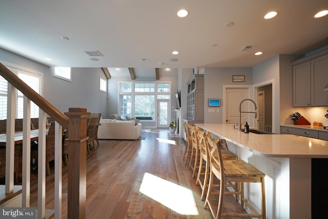 kitchen featuring a kitchen bar, sink, gray cabinets, a kitchen island with sink, and light hardwood / wood-style floors