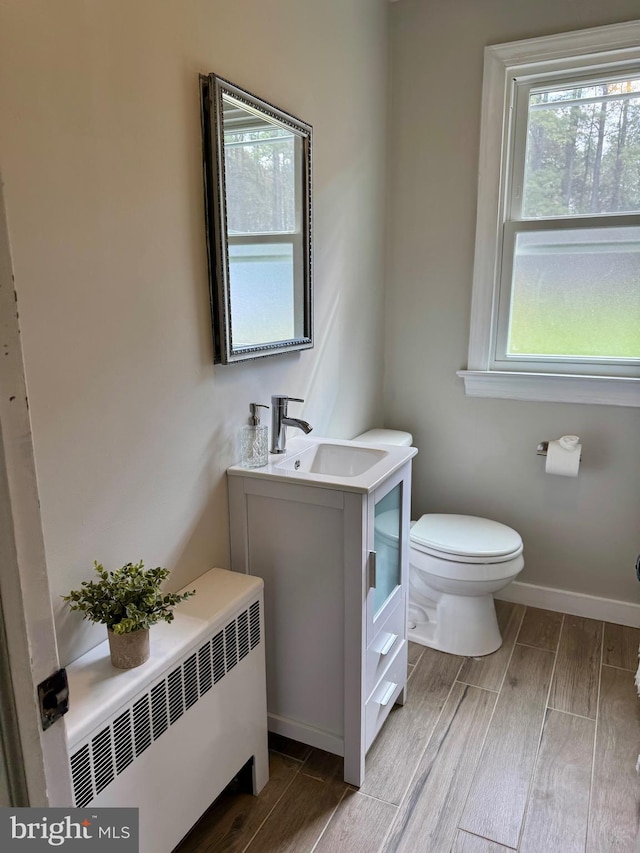 half bathroom with baseboards, toilet, radiator heating unit, wood finish floors, and vanity