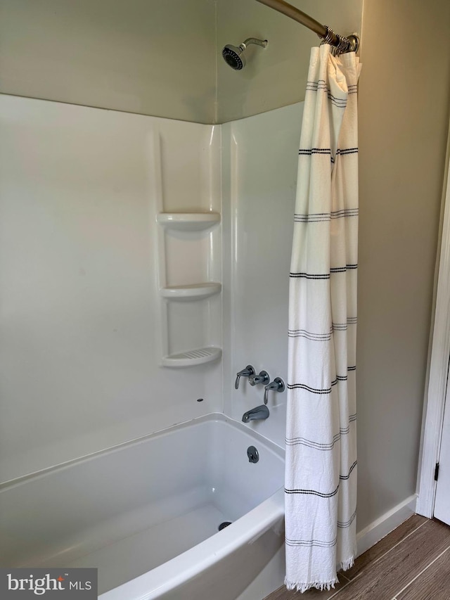 bathroom featuring baseboards, wood finished floors, and shower / tub combo with curtain