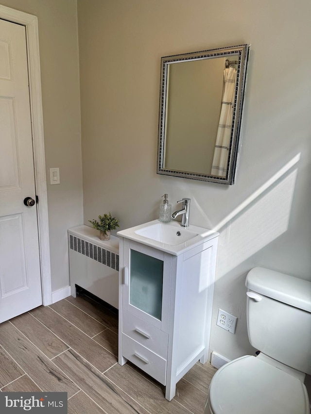 half bathroom with vanity, radiator, toilet, baseboards, and wood tiled floor
