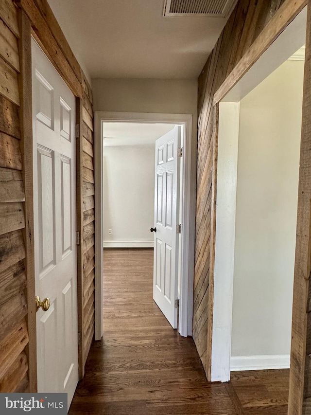 hallway featuring dark wood-style floors, visible vents, and wooden walls