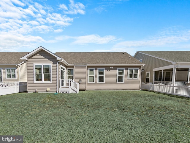 back of property with fence, a lawn, and roof with shingles