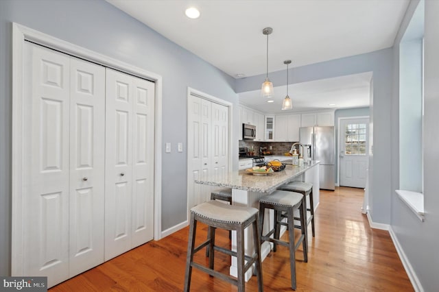 kitchen with decorative light fixtures, white cabinetry, a kitchen breakfast bar, a kitchen island with sink, and stainless steel appliances