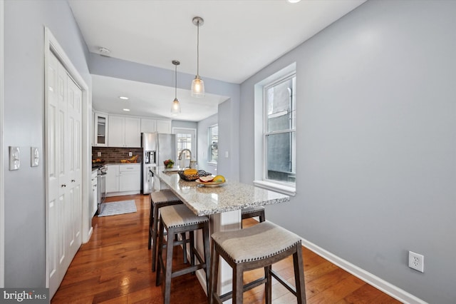 kitchen with dark wood-type flooring, decorative backsplash, hanging light fixtures, and white cabinets