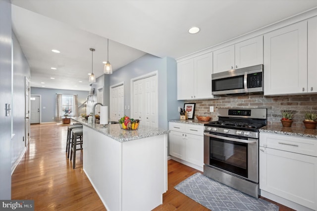 kitchen with pendant lighting, stainless steel appliances, light stone countertops, white cabinets, and a center island with sink