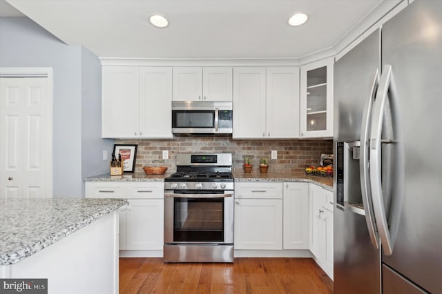 kitchen featuring appliances with stainless steel finishes, white cabinets, decorative backsplash, light stone countertops, and light wood-type flooring