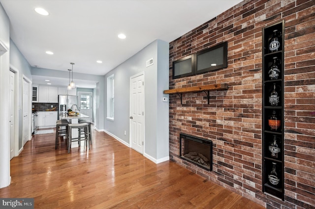 interior space with a breakfast bar, decorative light fixtures, white cabinetry, wood-type flooring, and a brick fireplace