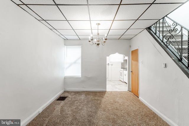 unfurnished dining area with light carpet, a notable chandelier, and a drop ceiling