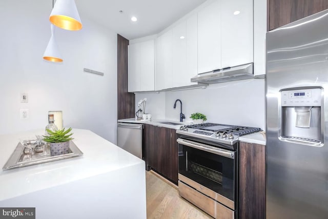 kitchen with appliances with stainless steel finishes, decorative light fixtures, white cabinetry, dark brown cabinets, and light wood-type flooring