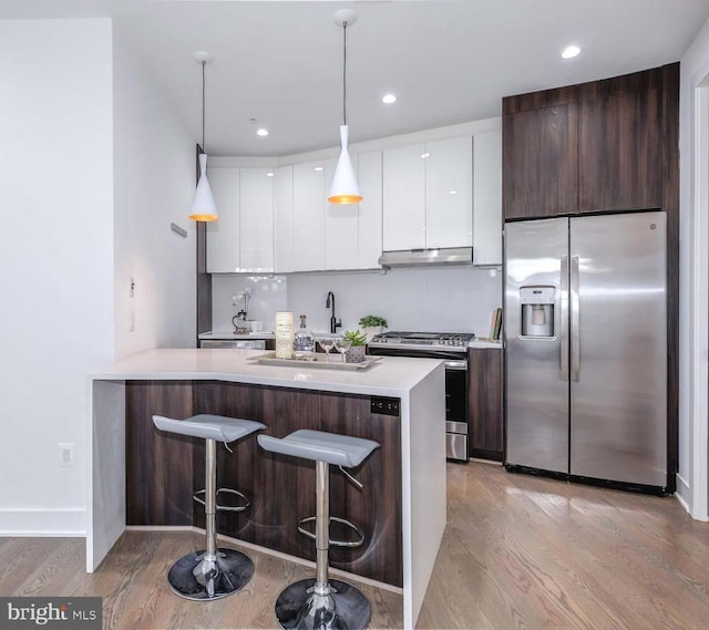 kitchen featuring appliances with stainless steel finishes, a breakfast bar, pendant lighting, white cabinetry, and dark brown cabinets