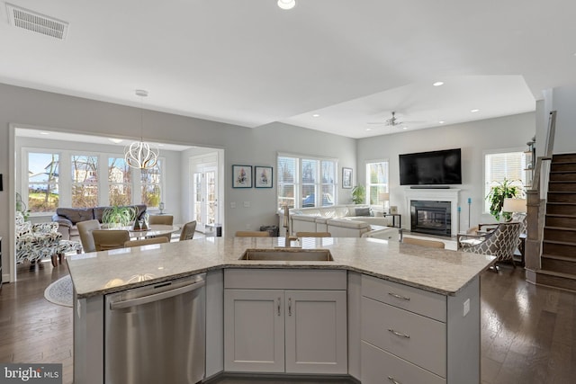 kitchen featuring an island with sink, hanging light fixtures, sink, stainless steel dishwasher, and light stone counters