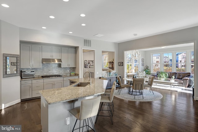 kitchen with a center island with sink, hanging light fixtures, light stone countertops, sink, and a kitchen bar