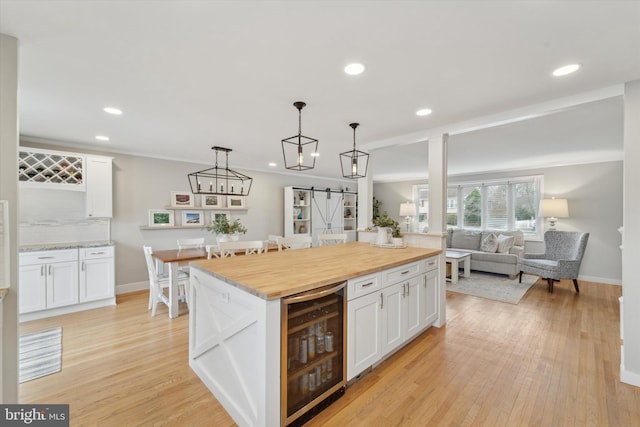 kitchen with wine cooler, white cabinets, wood counters, decorative light fixtures, and a barn door